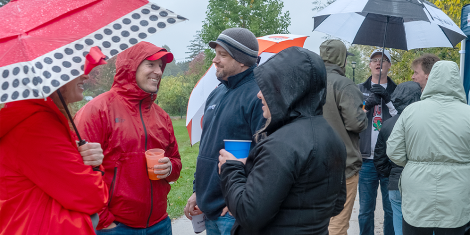 Alumni gather and reconnect holding umbrellas on Saturday